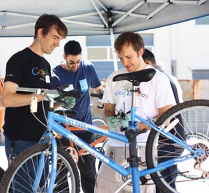 Three volunteer mechanics under a canopy repairing a bike