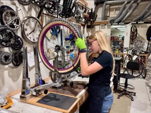 Young woman truing a wheel in the SVBE shop.  Wheel on truing stand.