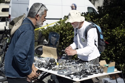 Buyer and seller outdoors at a table holding many bicycle parts and accessories